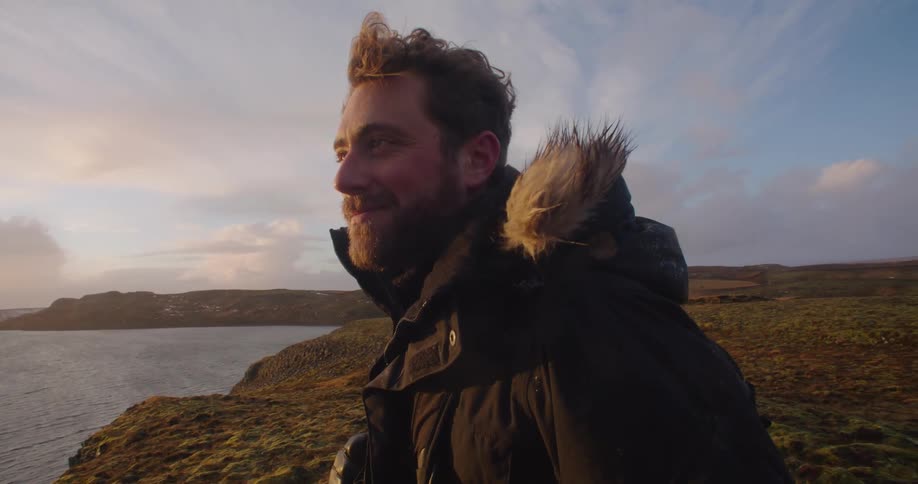 A man is outdoors by the coast while the sun is settting