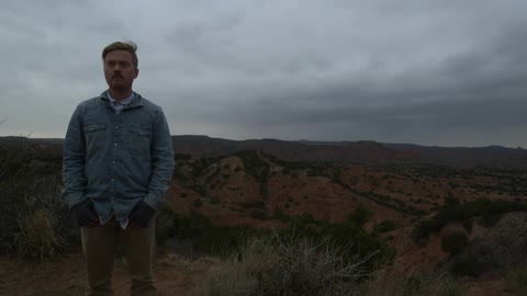 A man stands in front of a cloudy and remote background