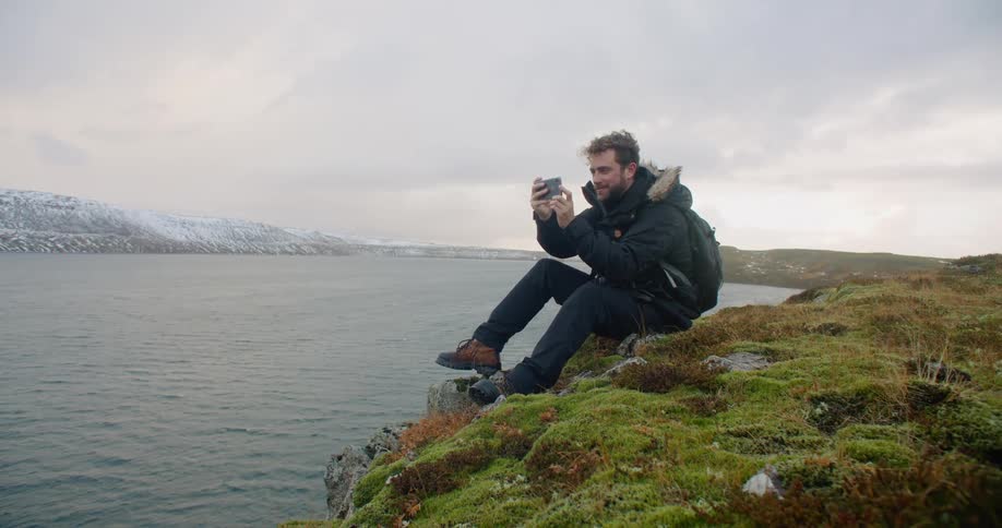 A man is sitting on the beach coast and taking pictures