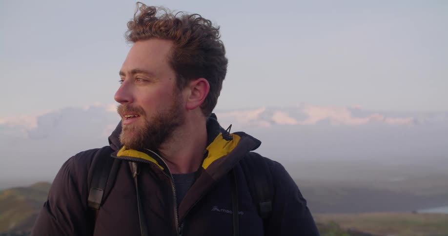A man is standing on a cliff near water and smiling