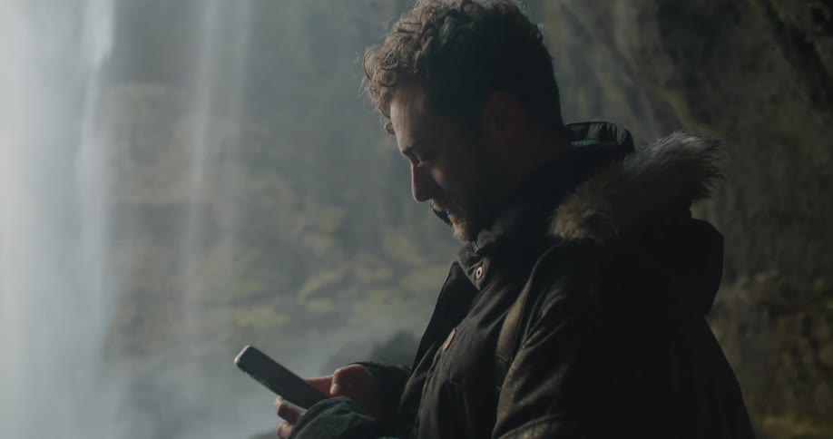 A man is taking photos of a waterfall with his cellphone