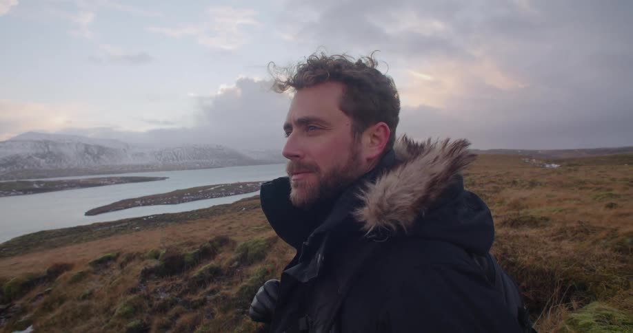 A man is deep in thought as he looks around him at the water and mountains
