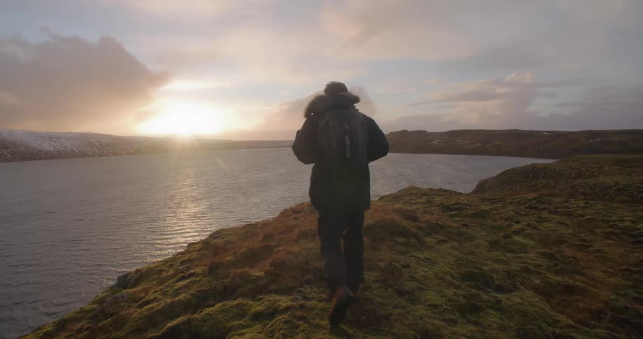 A man is walking on the coast by a body of water at dusk