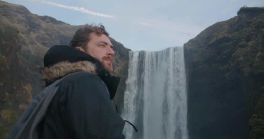 A man hiking near a large waterfall in nature on a cold day