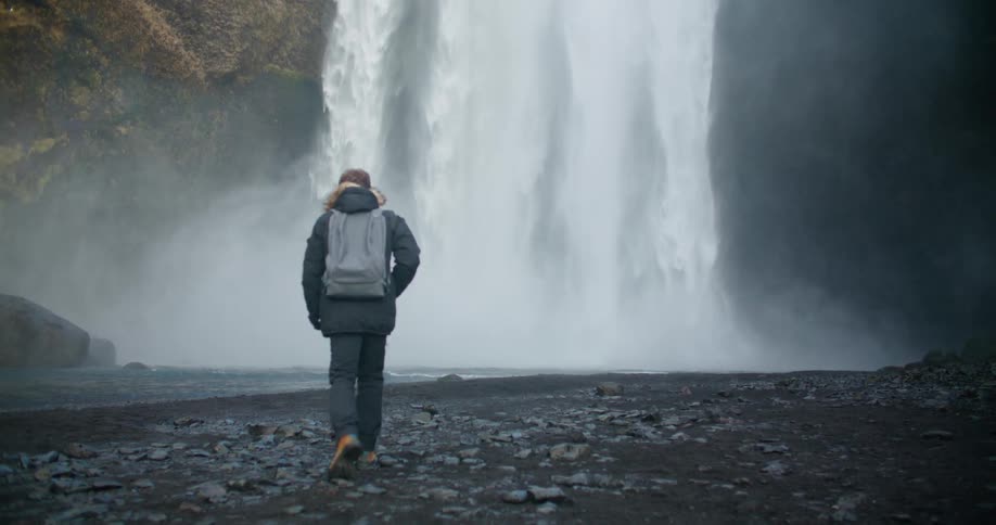 A man hiking near a large waterfall on a cold misty day