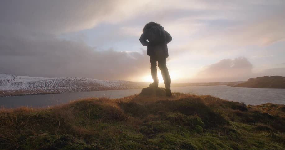 A man is hiking on the coast of a beach at dusk