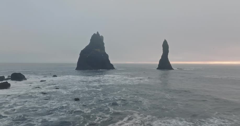 A landscape view of rock formations in the ocean with waves flowing to the shore