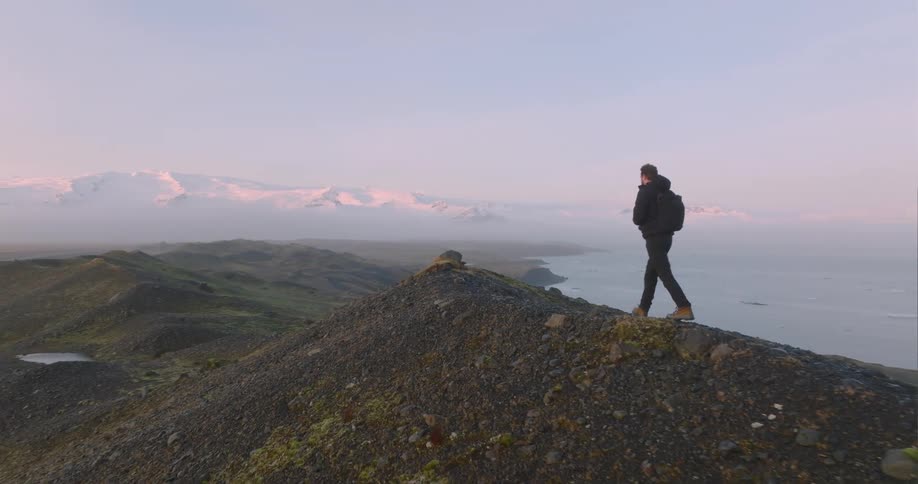 A man walks along a narrow ridge high above the ocean coast