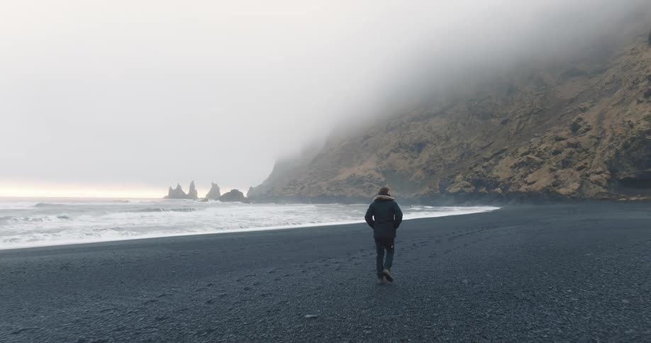 Young man walking on the reynisfjara black sand beach at sunset