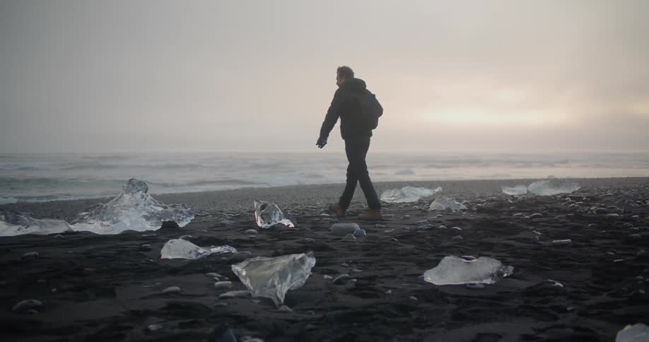 A man walks across a shore with large pieces of ice