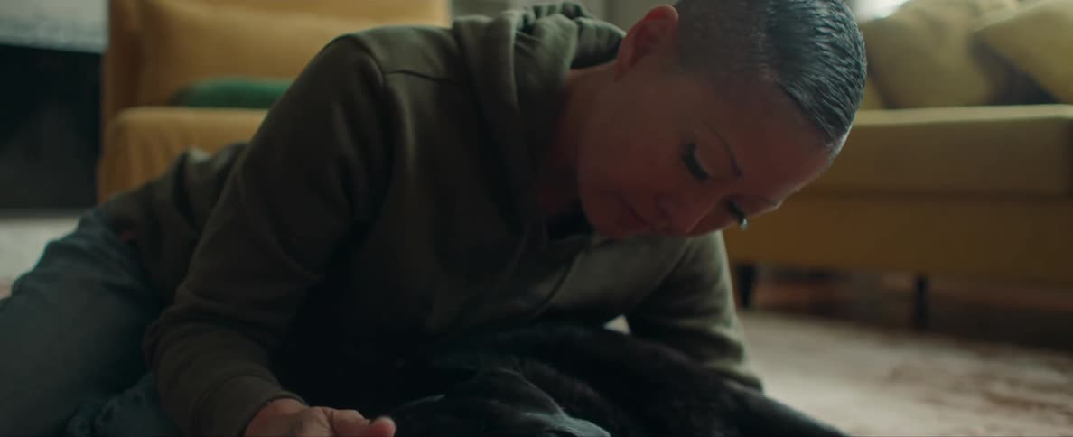 Young woman laying on the living room floor caressing the head of a black dog