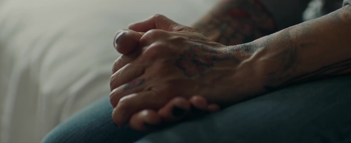Person with tattooed arms and hands sitting on a bed rubbing his hands together