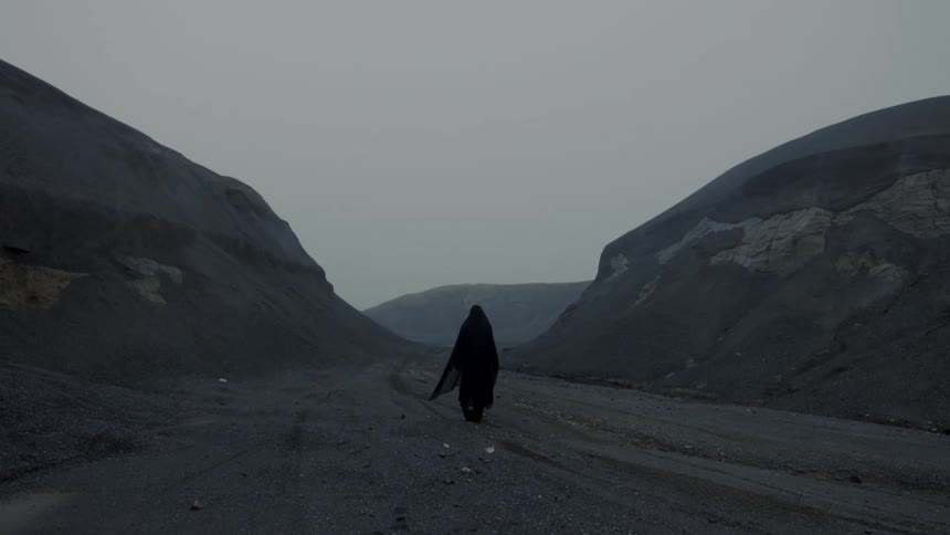 Someone wearing a black cloak is walking on a mountain road