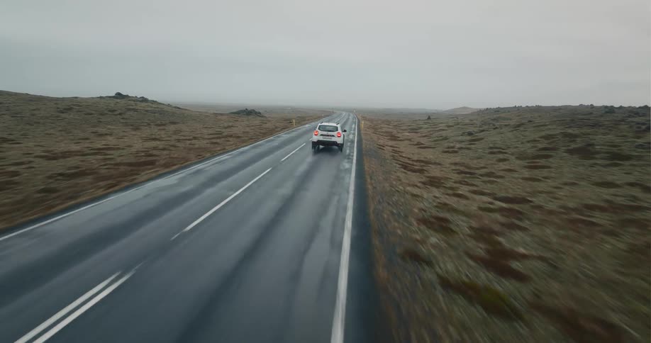 A vehicle travels along a road through a vast countryside on a cloudy day