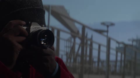 Male photographer stands near brick wall taking pictures as it snows