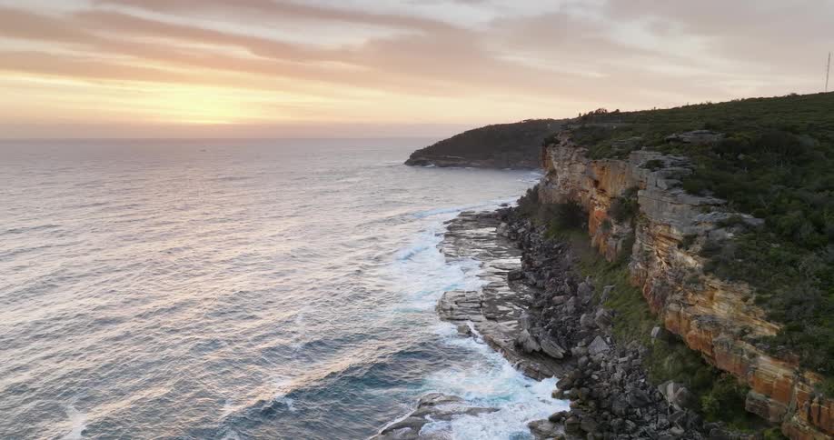 Aerial view of ocean waves crashing on rocky shore at sunset