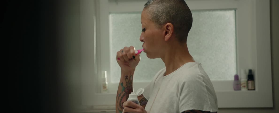 A woman is in the bathroom and is brushing her teeth
