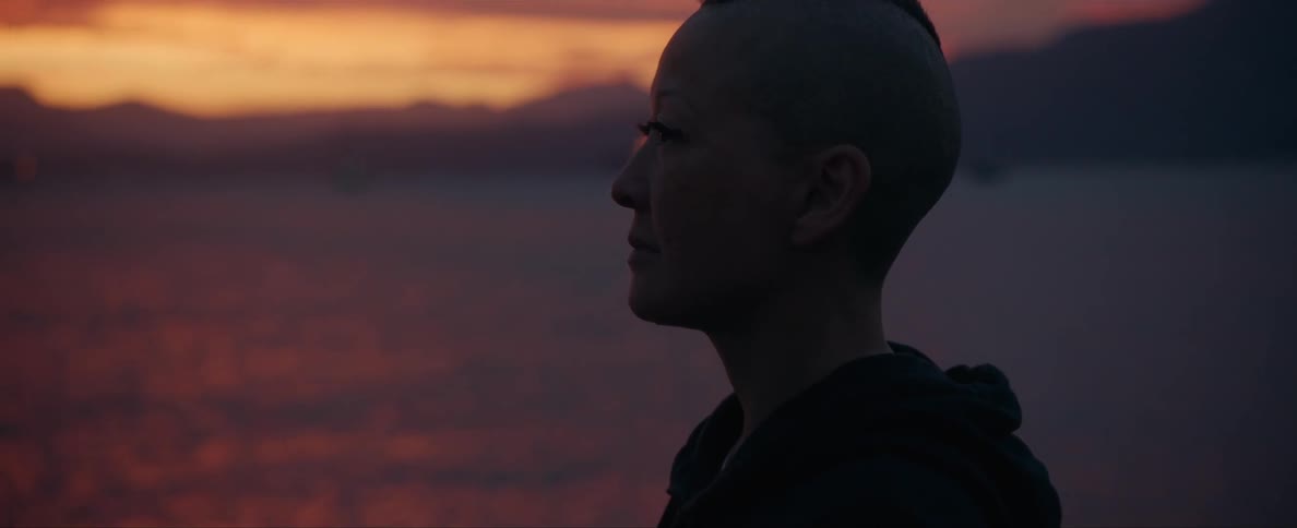 A woman is standing outdoors and watching the sunset