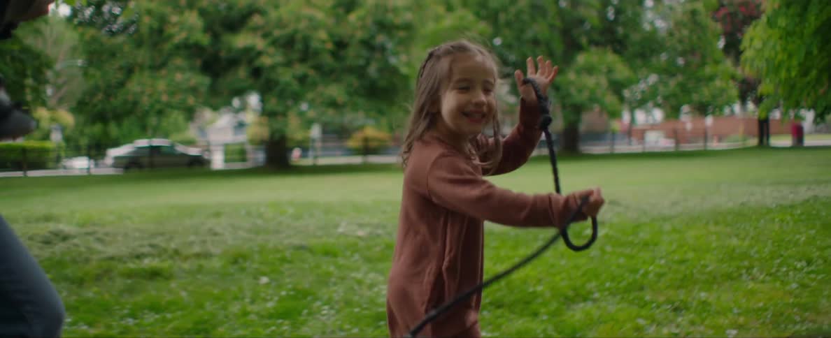 A little girl is holding a dog leash as she runs and turns to look behind her