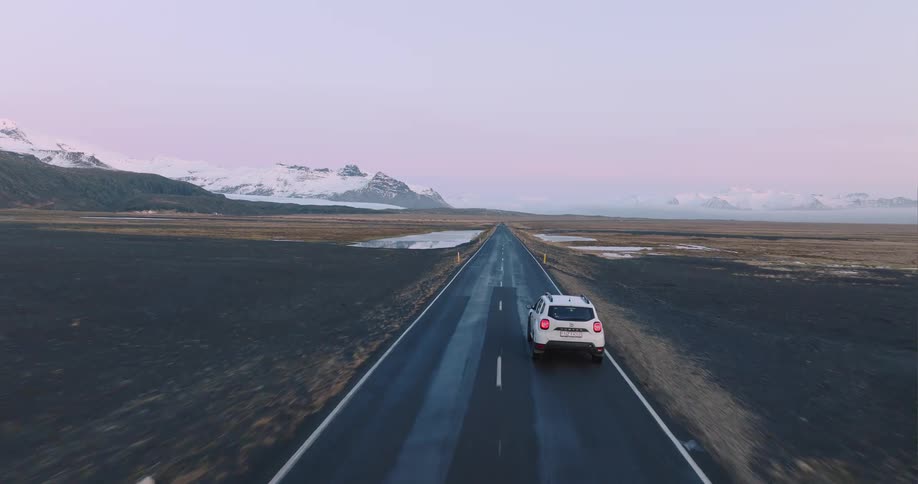 An automobile travels on an open road with snow covered mountains in the distance