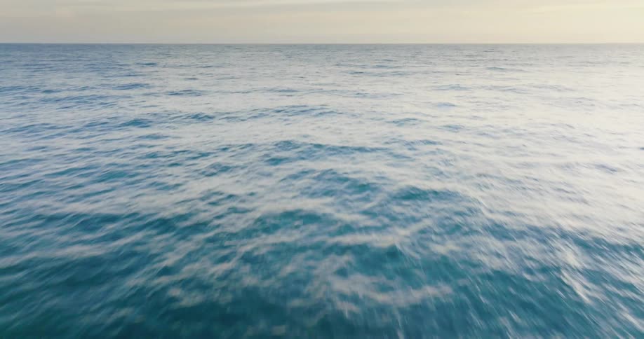 Aerial view of the ocean then revealing clouds at sunrise