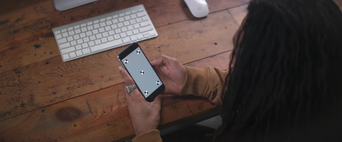 A man who is sitting at a desk pulls out a cell phone and is holding it