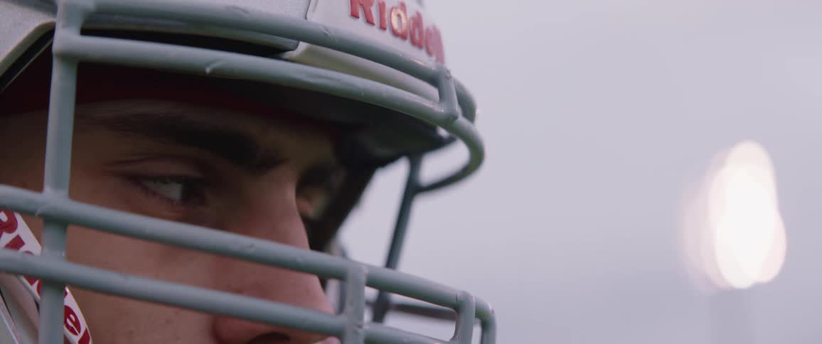 A teenage boy wearing a football helmet appears to be thinking