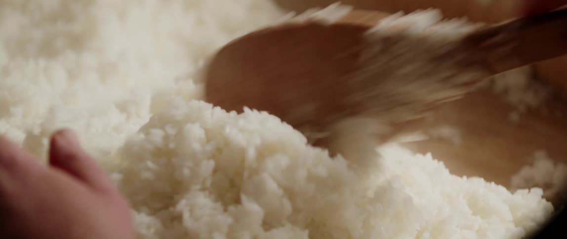 Cook stirs mass of rice on wooden surface using large wide wooden spoon