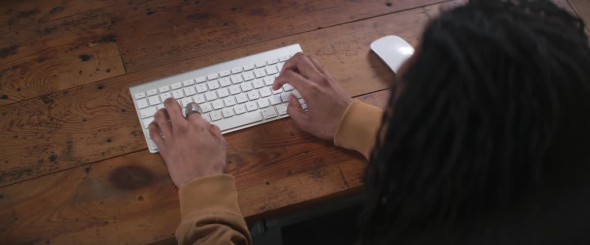 Man sitting at a wooden desk typing on a white wireless keyboard