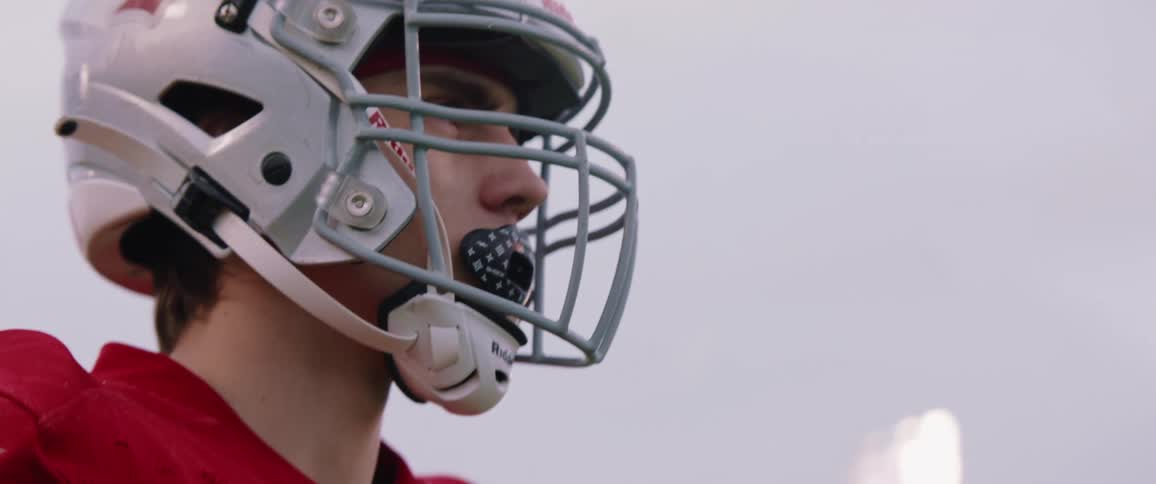 Young football player wearing a football helmet in a football field at evening