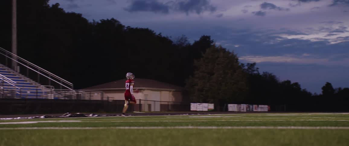 A man is practicing football outdoors at dusk