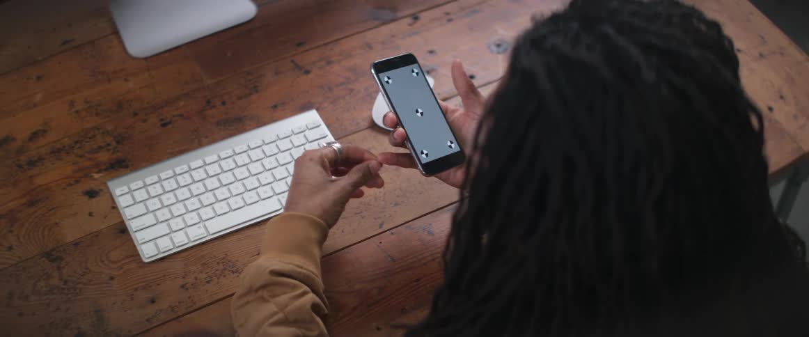 A man is sitting at a desk and holding a cell phone while talking