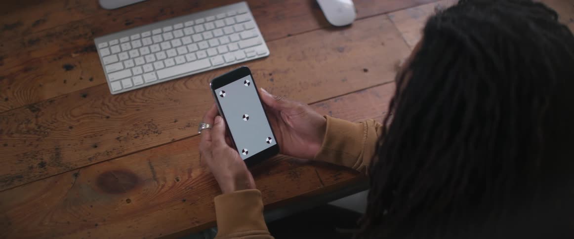Man with brown jacket and braids sitting at desk uses smartphone