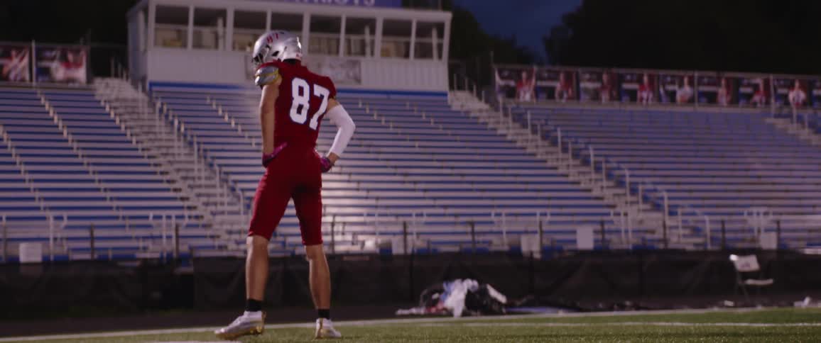 A football player is wearing full gear and pacing on a football field at night