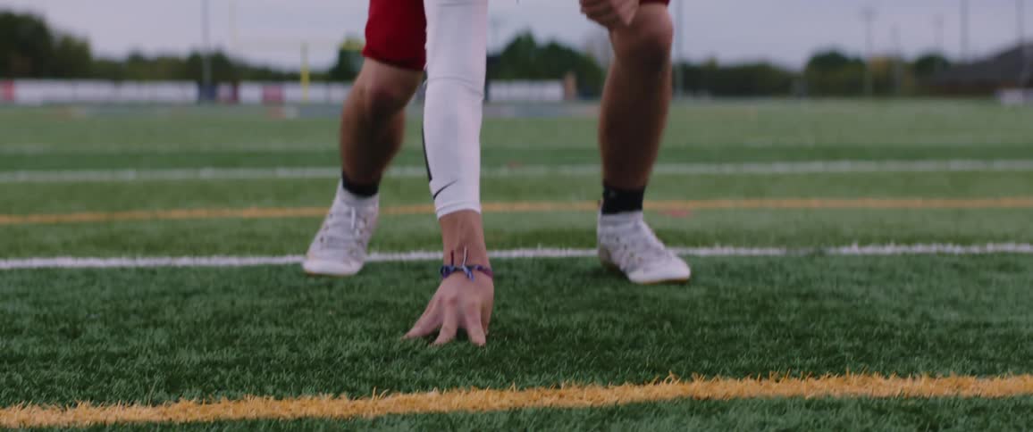 A teenage boy bends down and puts his hand on the field as he plays football