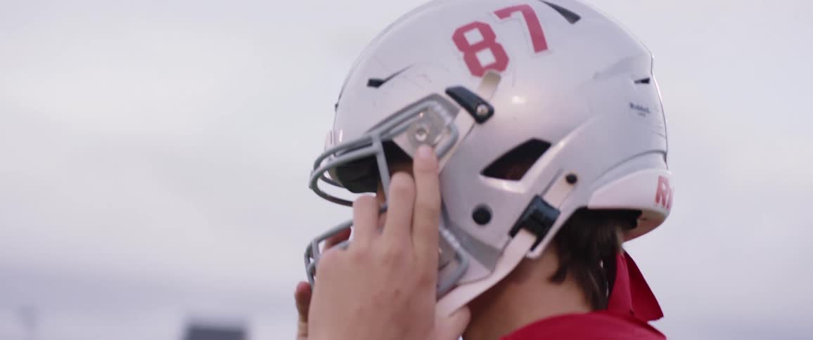 Youth puts on football helmet standing on sports field under lights
