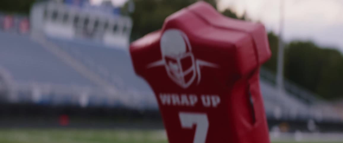 Male player with red jersey does the sled push in american football stadium