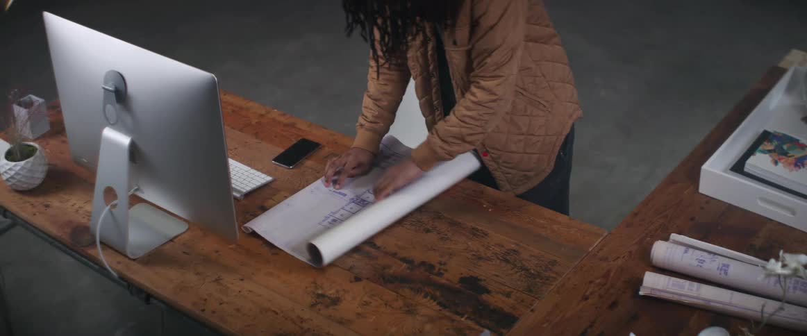 A man rolls out blueprints while standing at his desk
