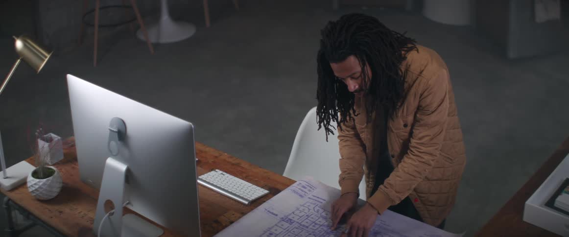 A man stands at his desk in his office and examines a blueprint