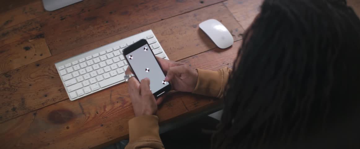 Person sits at wooden desk near keyboard texting on mobile phone