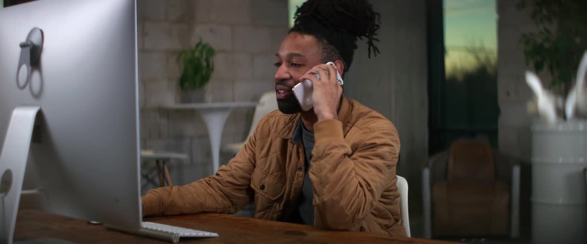 A man smiling and nodding while talking on a cell phone in front of a computer