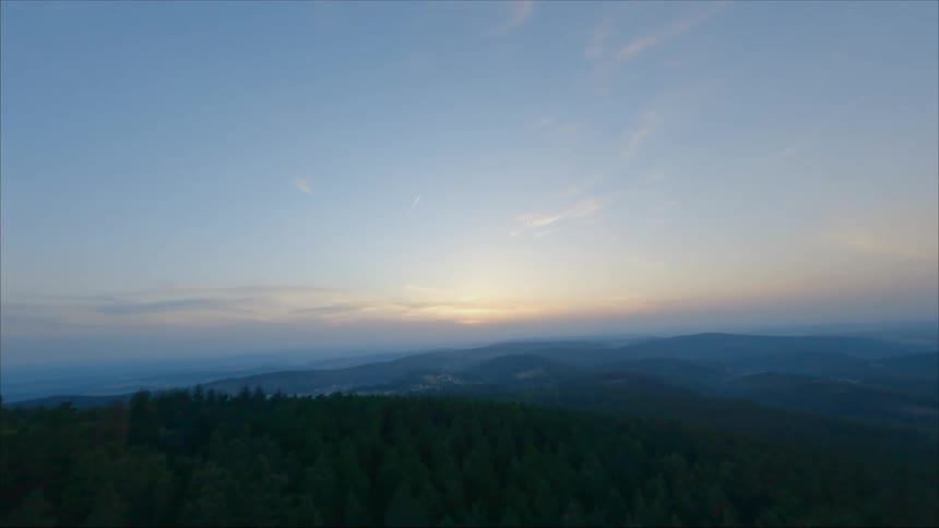 Aerial view of forest being silhouetted on hill against the sunset