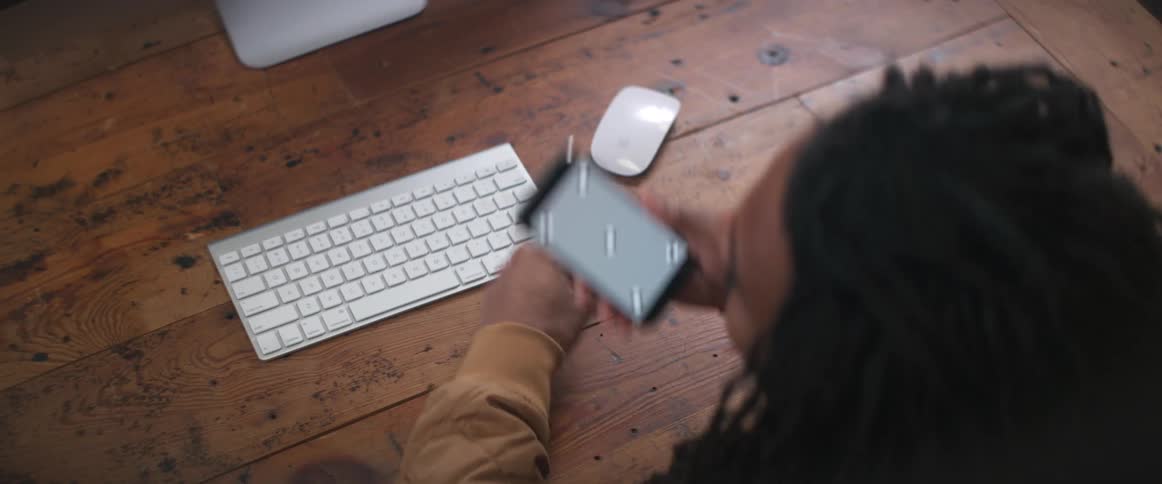 Young man sitting on a wooden desk in front of a computer picks up a phone with replaceable screen