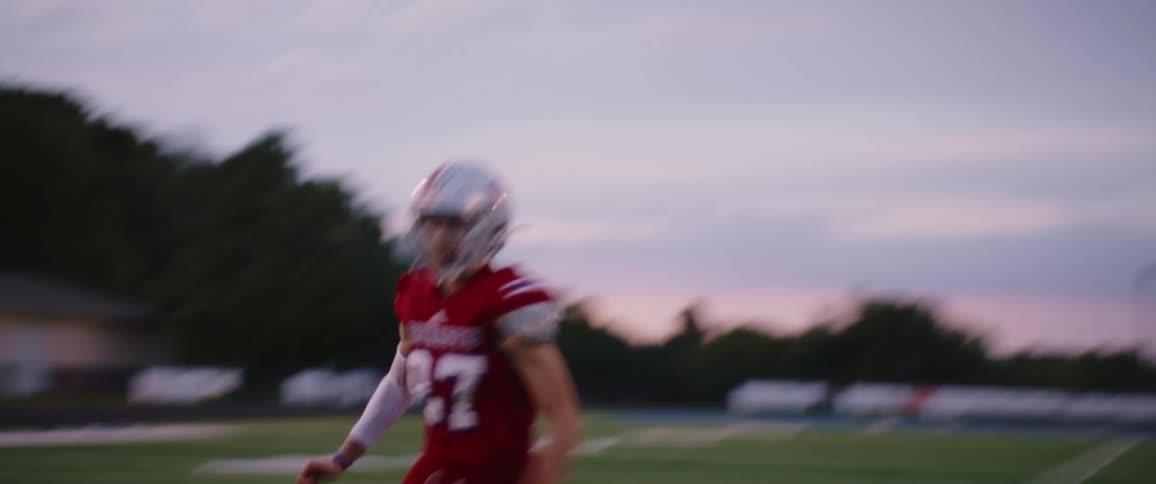A man is catching a football on the field at dusk