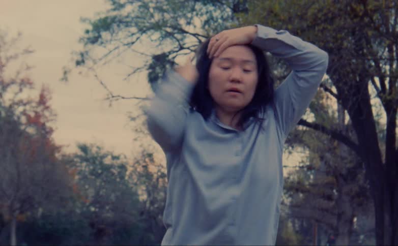 A woman outside runs her hands through her hair and then does jerky arm movements across her body