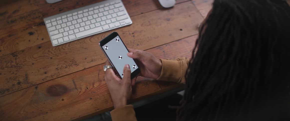 Woman with curly hair and yellow sweater sits at desk using smartphone