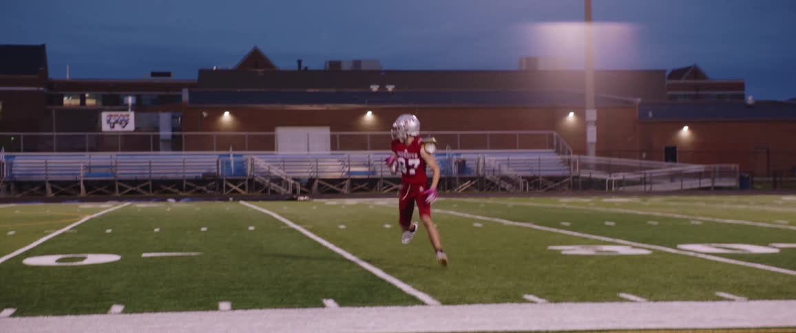 Football player runs across field and catches football during practice at night