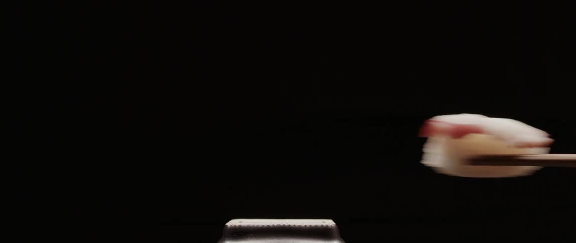 A piece of sushi being picked up with wood chopsticks
