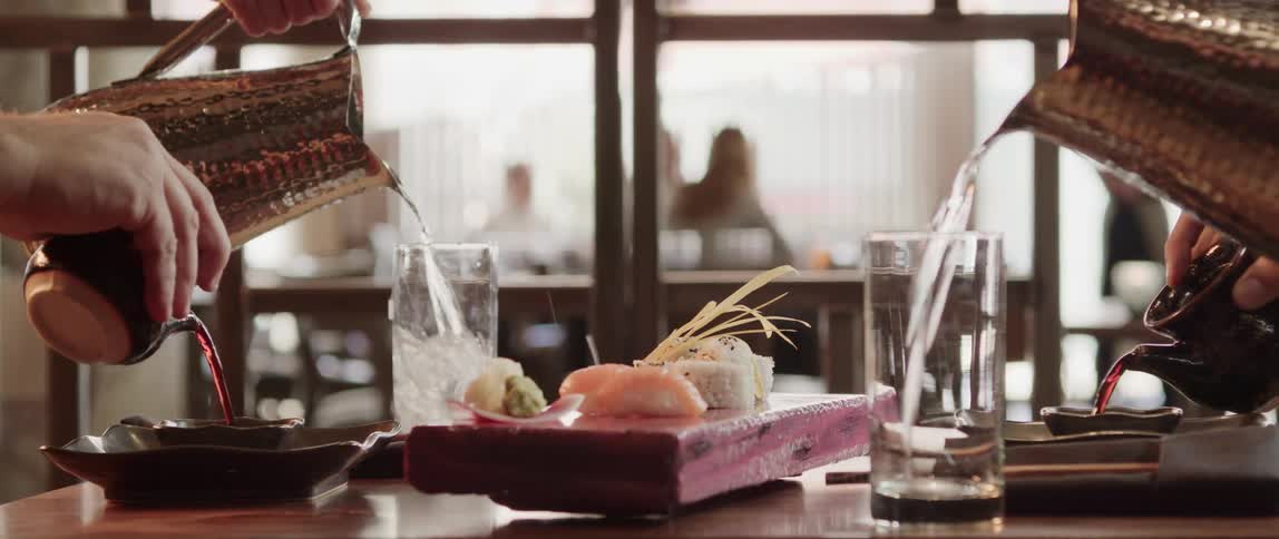 A server delivers sushi to two people at a table as water is poured in their glasses
