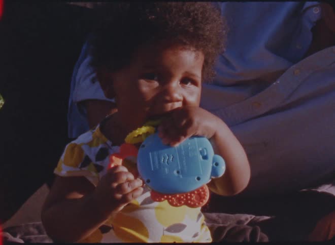 Vintage footage of a father lying on a blanket with his daughter as she chews on a toy